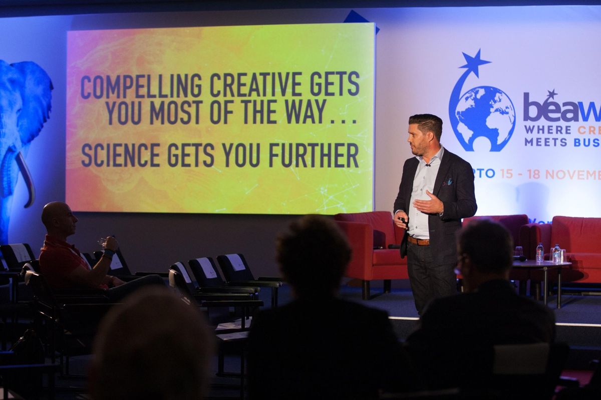 Ben on stage at BEAW in Porto beside a slide reading compelling creative gets you most of the way, science gets you further